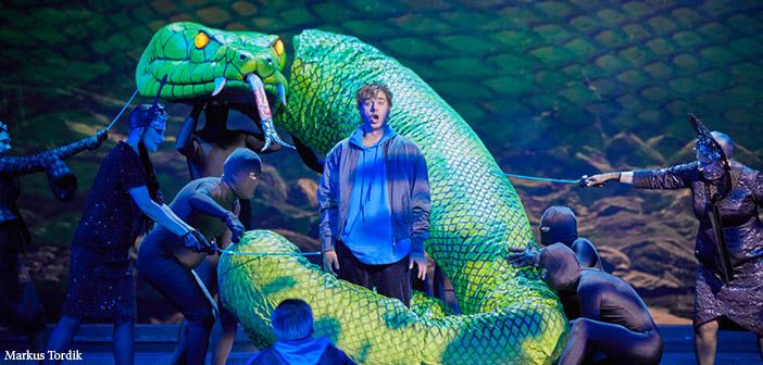 performer surrounded by snake prop operated by other performers