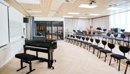 performing arts school music classroom with a piano, other instruments in background, and rows of chairs