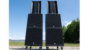 Two tall black professional speaker stacks positioned outdoors against blue sky and green landscape