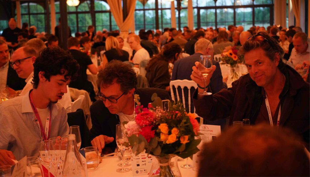 Busy formal dinner event with attendees at tables raising glasses in warm ambient lighting