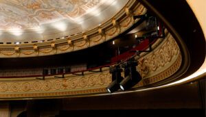 Curved theatre balcony with intricate ornamentation, and technical equipment including two stage light fixtures