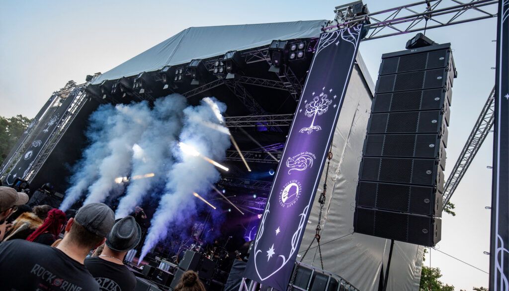 Large outdoor music festival stage with line array speakers and crowd watching performance