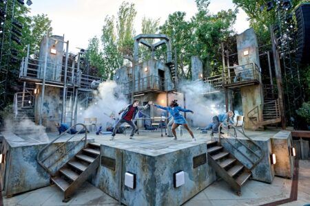 Outdoor theatre with actors reaching to each other on industrial-look set