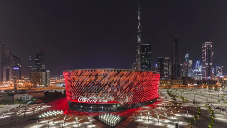 Illuminated red arena at night with city skyline background