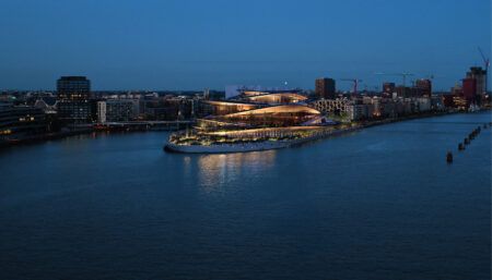 Designer chosen for new Hamburg State Opera venue Illuminated building on waterfront peninsula at dusk