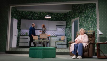 Theatre stage set with man and woman talking in kitchen, and older woman in armchair