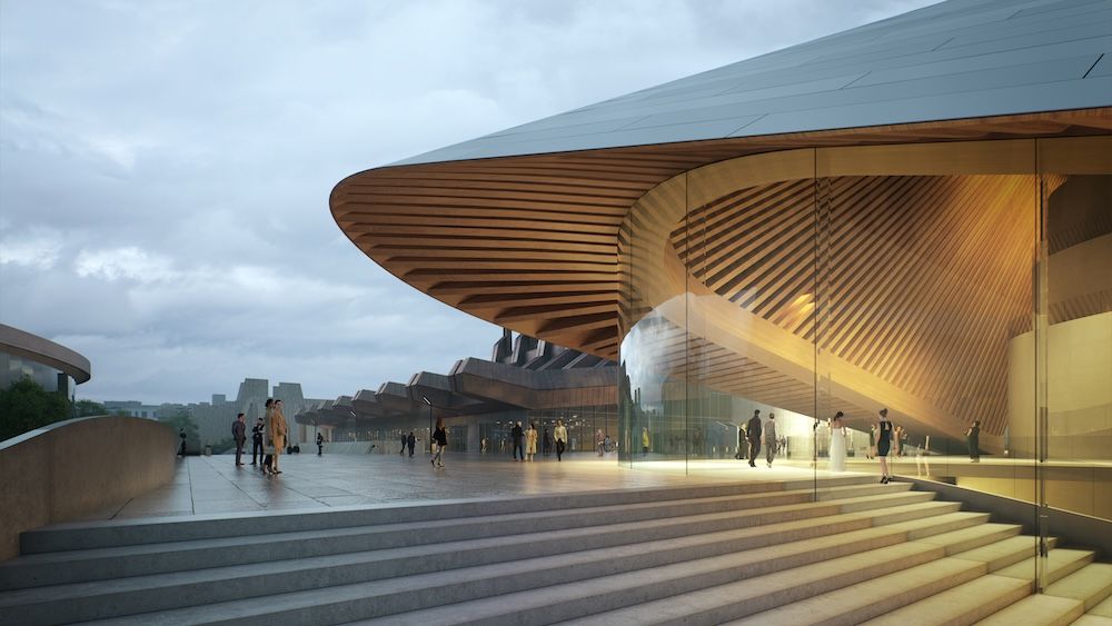Exterior view of The Opera & Ballet Theatre of Kosovo showing a dramatic curved entrance canopy with horizontal slats, glass curtain walls, and wide stone steps leading to the foyer, with people gathering on the plaza under an overcast sky.