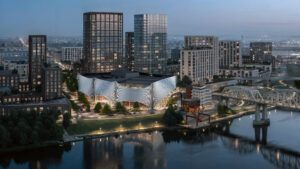 Architectural rendering showing an aerial night-time view of the new Tennessee Performing Arts Center, a sculptural building with an undulating aluminium tube facade, situated on the East Bank of the Cumberland River in Nashville, surrounded by parkland and new residential development.