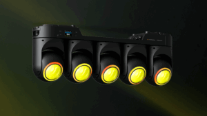 The Ayrton MagicBlade Neo modular linear fixture shown against a dark green background, with five moving heads emitting yellow light.