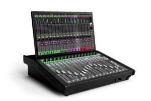 Angled view of the Solid State Logic TCA Tour, a black desktop mixing console with 16 white faders, illuminated green select buttons, and a large touchscreen display above the fader bank showing colour-coded channel strips and meters