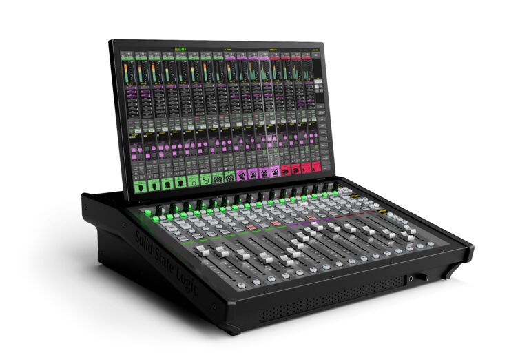 Angled view of the Solid State Logic TCA Tour, a black desktop mixing console with 16 white faders, illuminated green select buttons, and a large touchscreen display above the fader bank showing colour-coded channel strips and meters
