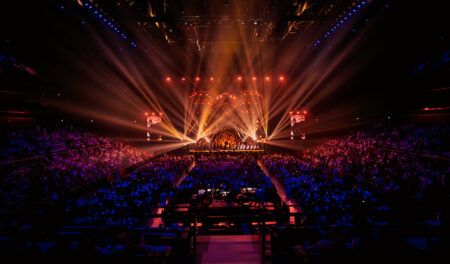 Dubai’s Coca-Cola Arena upgrades to DirectOut Prodigy.MP audio system Show at Coca-Cola Arena, with gold and red stage lighting illuminating performers on a distant stage and a mixing desk positioned in the crowd