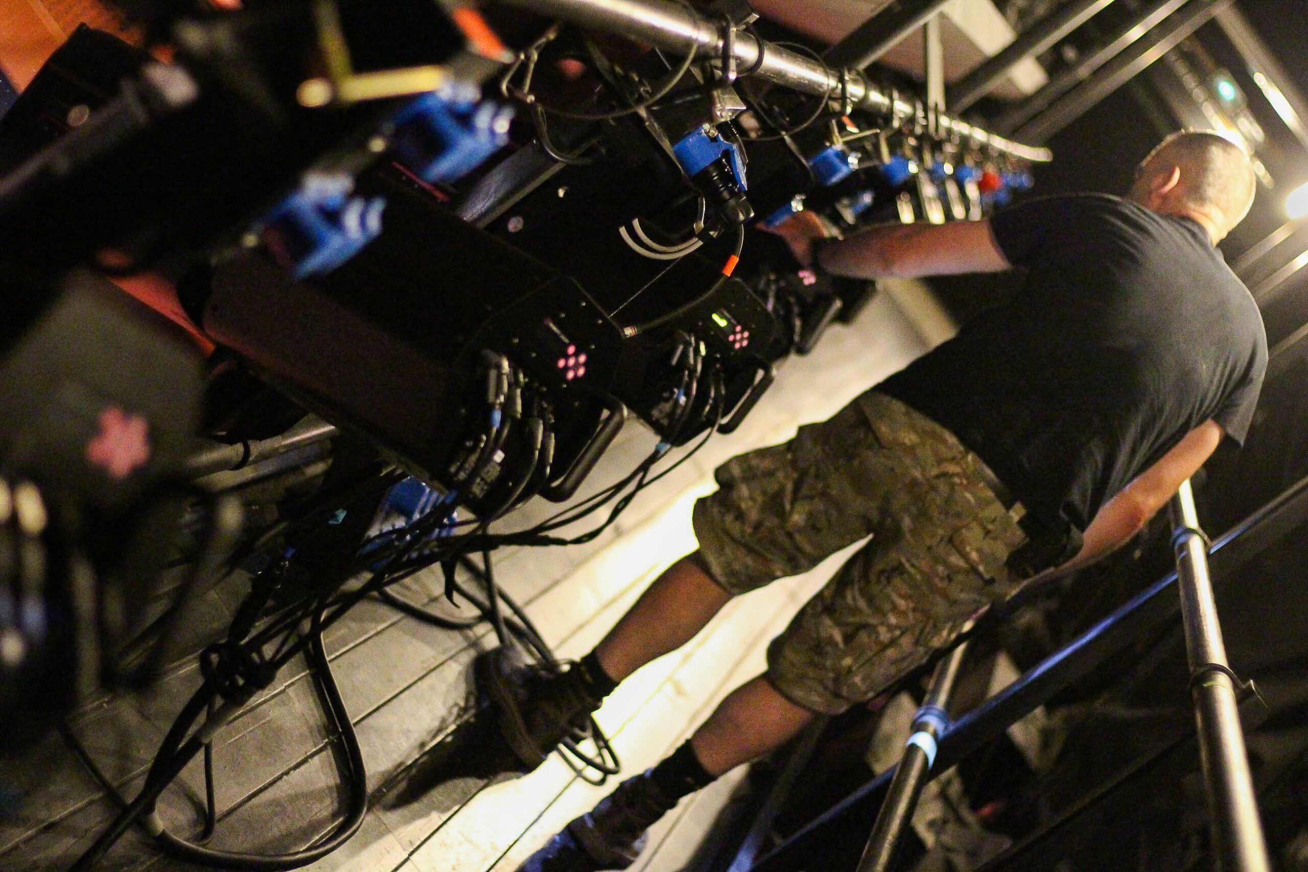 Close-up of several stage lighting fixtures mounted on an overhead bar with a technician working among them