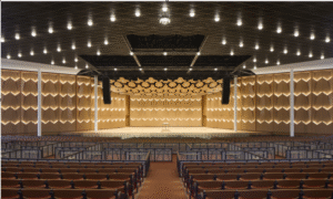 Interior of Ravinia’s Hunter Pavilion showing the illuminated chevron-patterned acoustical shell walls surrounding the stage, with rows of seating in the foreground